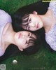 A couple of young women laying on top of a lush green field.