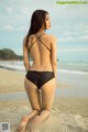 A woman in a black bikini sitting on a beach.