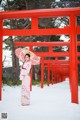 A woman in a pink kimono holding an umbrella in front of a red gate.