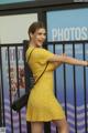 A woman in a yellow dress posing in front of a fence.