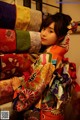 A woman in a colorful kimono standing in front of a pile of fabric.