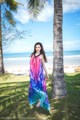 A woman in a colorful dress standing next to a palm tree.