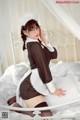 A woman in a maid outfit is sitting on a bed.