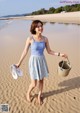 A woman walking on the beach holding a basket and flip flops.