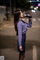 A woman in a purple shirt and blue skirt drinking from a bottle.