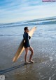 A woman standing on a beach holding a surfboard.