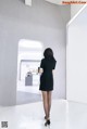 A woman in a black dress is walking through a white room.