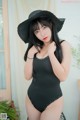 A woman in a black bathing suit and a black hat.