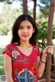 A woman in a red shirt leaning against a tree.