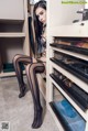 A woman in black stockings sitting on a shelf in a closet.