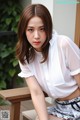 A woman sitting on a wooden bench wearing a white shirt.